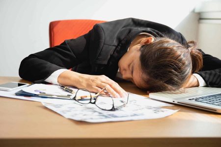 Masa başında önünde bilgisayarı ve işle ilgili raporları olan uyuyan bir kadın.